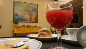 Una mesa de comedor con platos, un croissant, un vaso de jugo rojo y un cuadro en la pared.