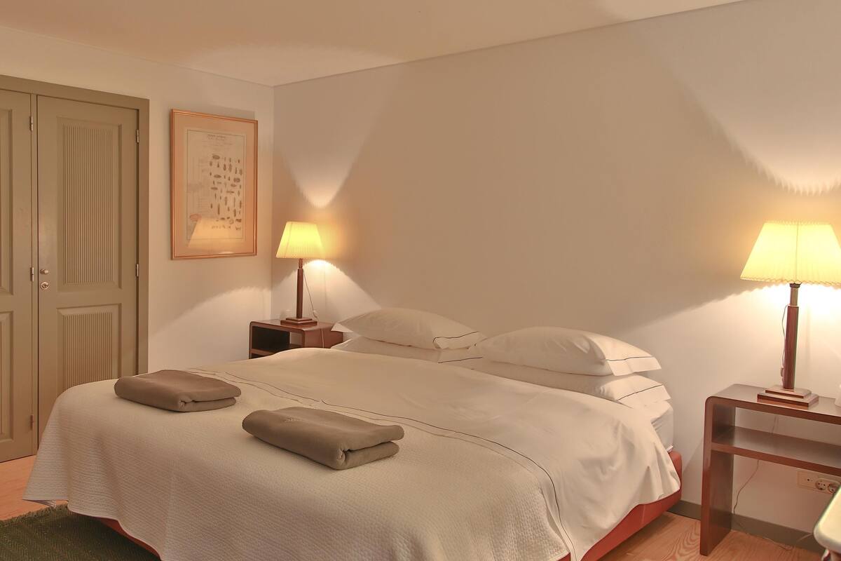 Une chambre d’hôtel avec un lit, deux lampes de chevet, une table de chevet, un tableau encadré au mur et une armoire.