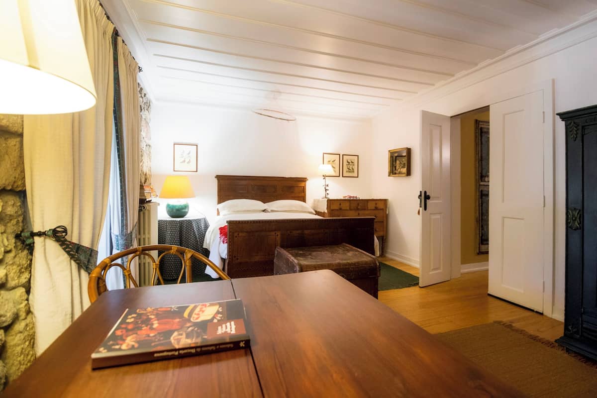 Une pièce avec une table en bois, un lit avec une tête de lit en bois, une table de chevet avec une lampe et un mur en pierre.