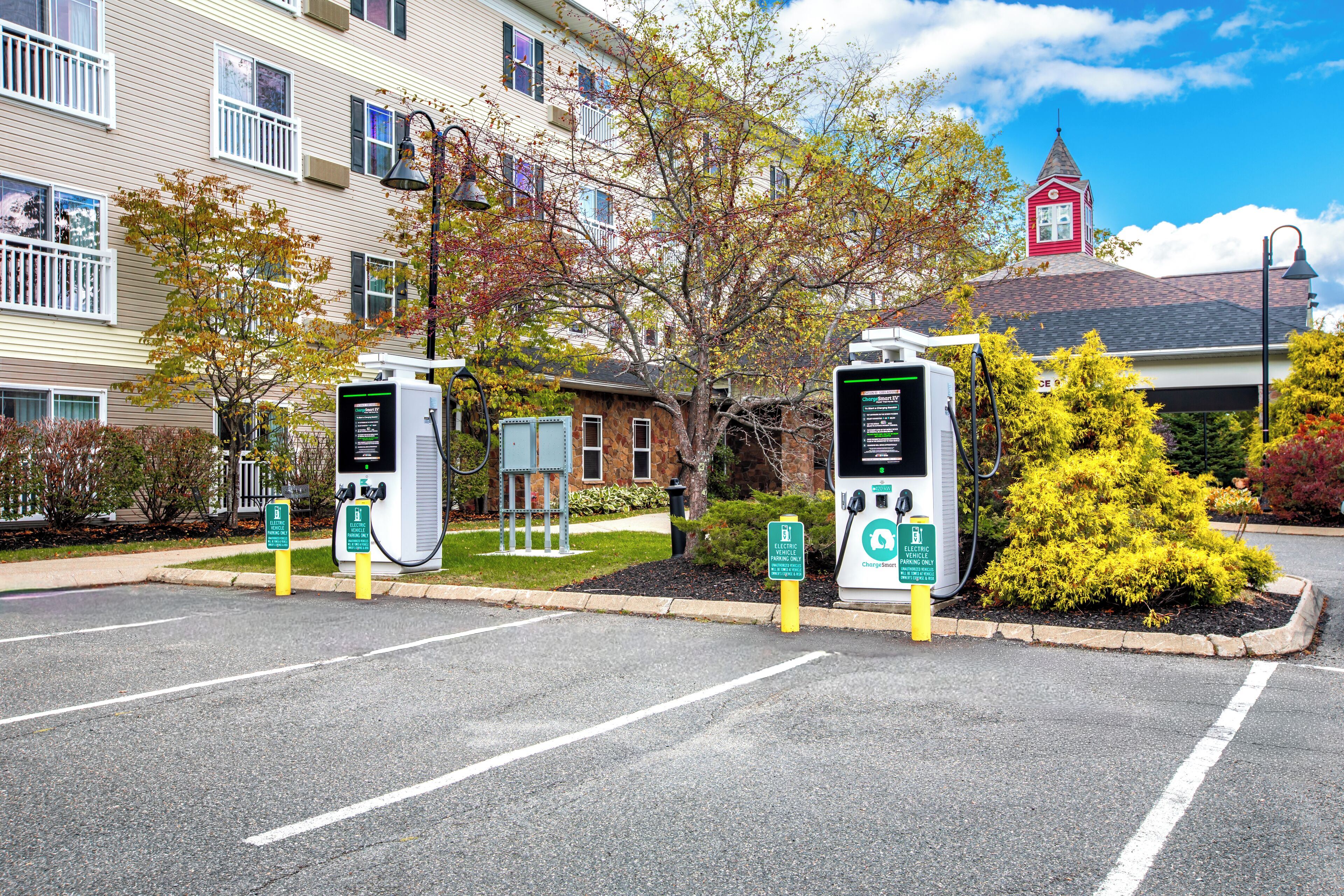A parking lot with electric vehicle charging stations, a building with a red tower, and a clear sky.
