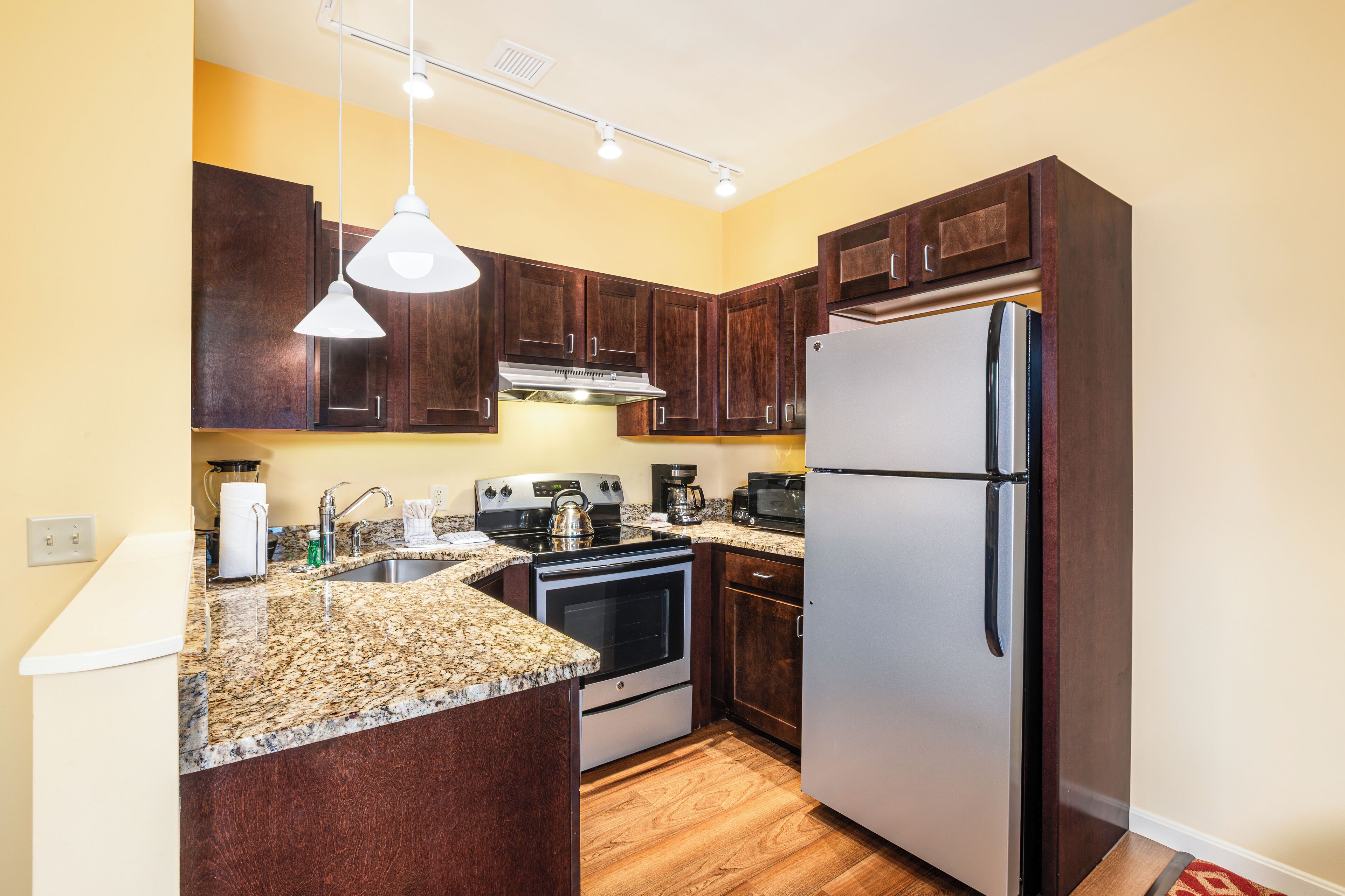 A kitchen with dark wooden cabinets, a stainless steel refrigerator, a built-in oven, a coffee maker, and a granite countertop.