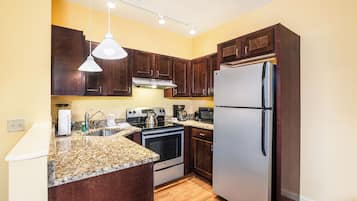 A kitchen with dark wooden cabinets, a stainless steel refrigerator, a built-in oven, a coffee maker, and a granite countertop.