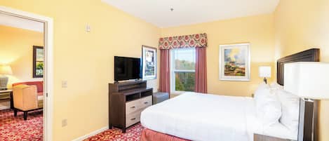 Habitación de hotel con una cama grande, televisión, escritorio con lámpara y ventana con cortinas.