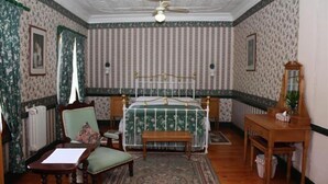 A bedroom with a bed, a chair, a table, a mirror, and a radiator. - The Royal Hotel (Pilgrims Rest)
