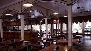 A restaurant with wooden tables and benches, a bar area, and large windows with curtains. - The Royal Hotel (Pilgrims Rest)