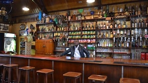 A bar with wooden shelves stocked with various bottles and snacks, a counter with stools, and a vintage decor. - The Royal Hotel (Pilgrims Rest)