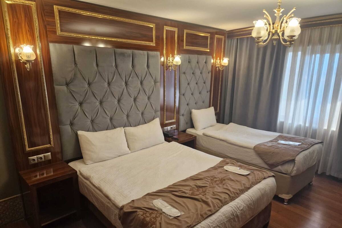 Une chambre d’hôtel avec deux lits, un lustre et une grande fenêtre avec des rideaux.