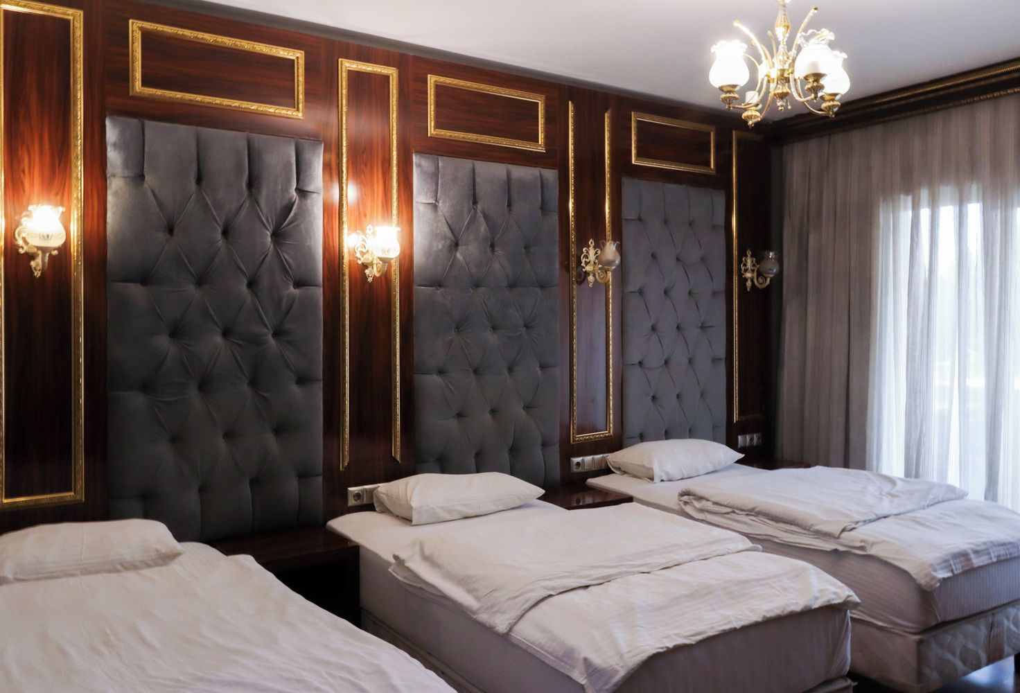 A hotel room with three beds, dark wood paneling, and a chandelier.