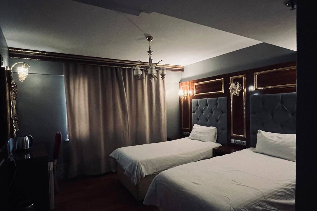 Une chambre d’hôtel avec deux lits, un lustre et une grande fenêtre avec des rideaux.