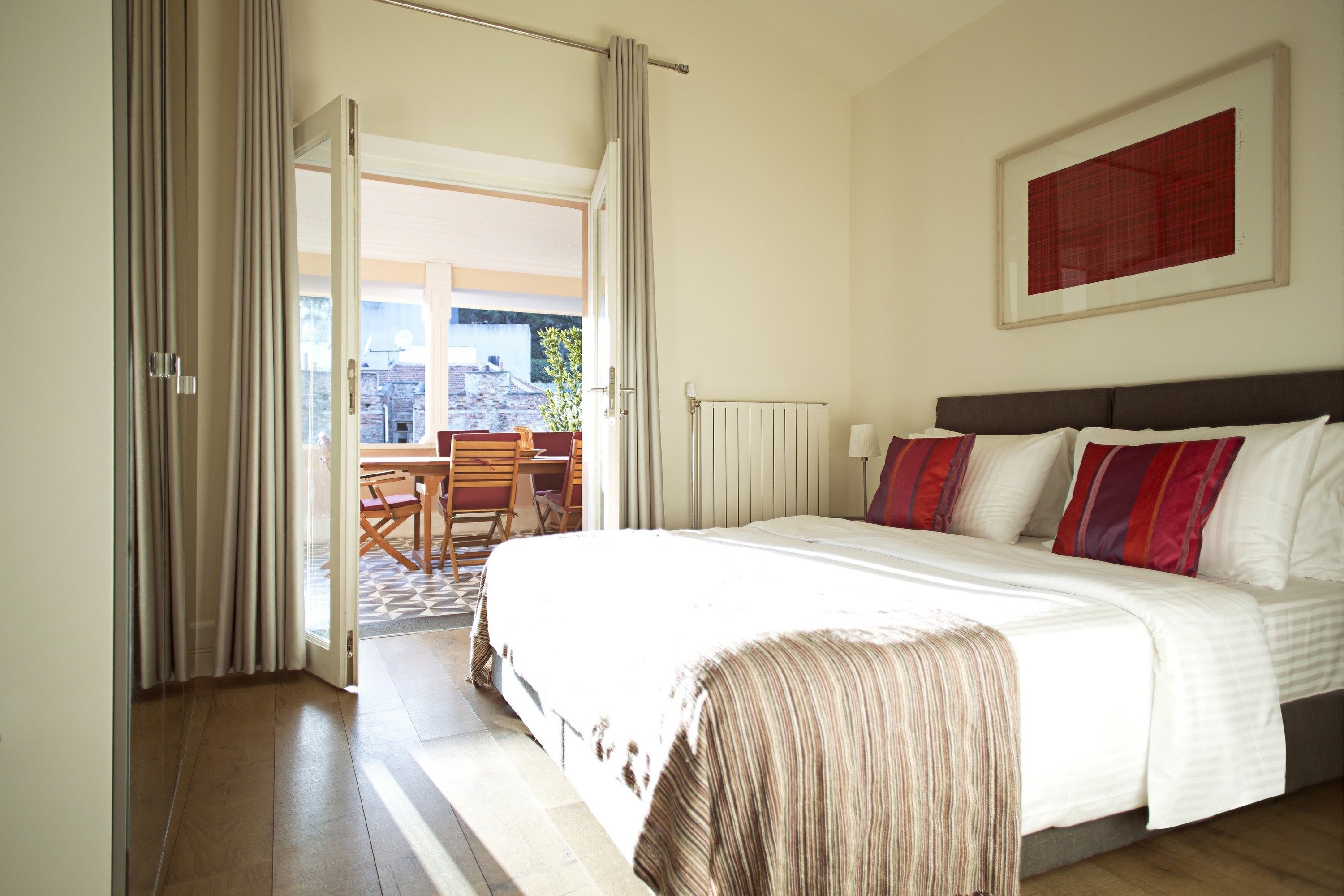 A hotel room with a large bed, a view to the outside, a dining area, and a framed picture on the wall.