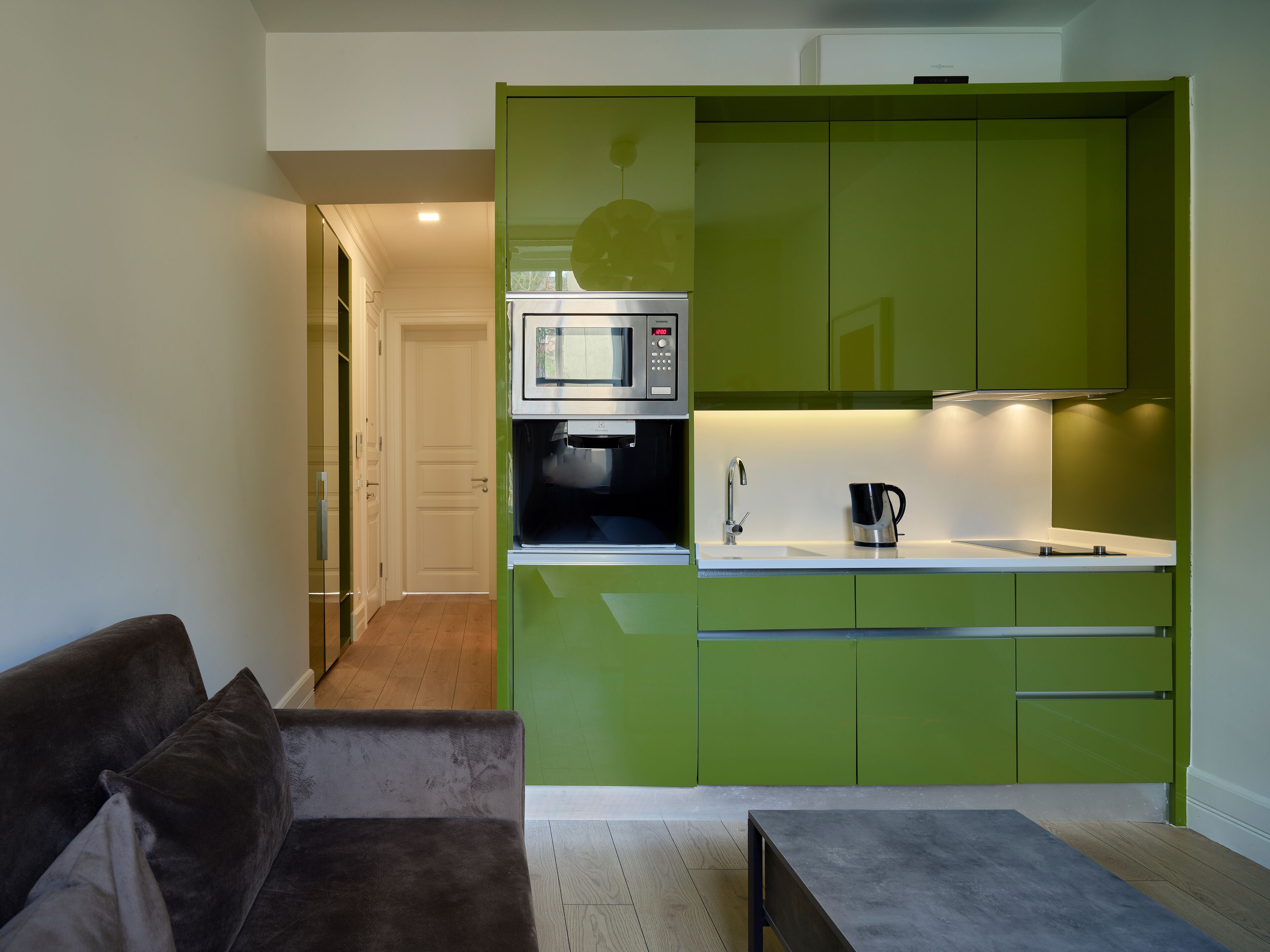 A compact kitchen with green cabinets, a microwave, a coffee maker, and a small countertop.