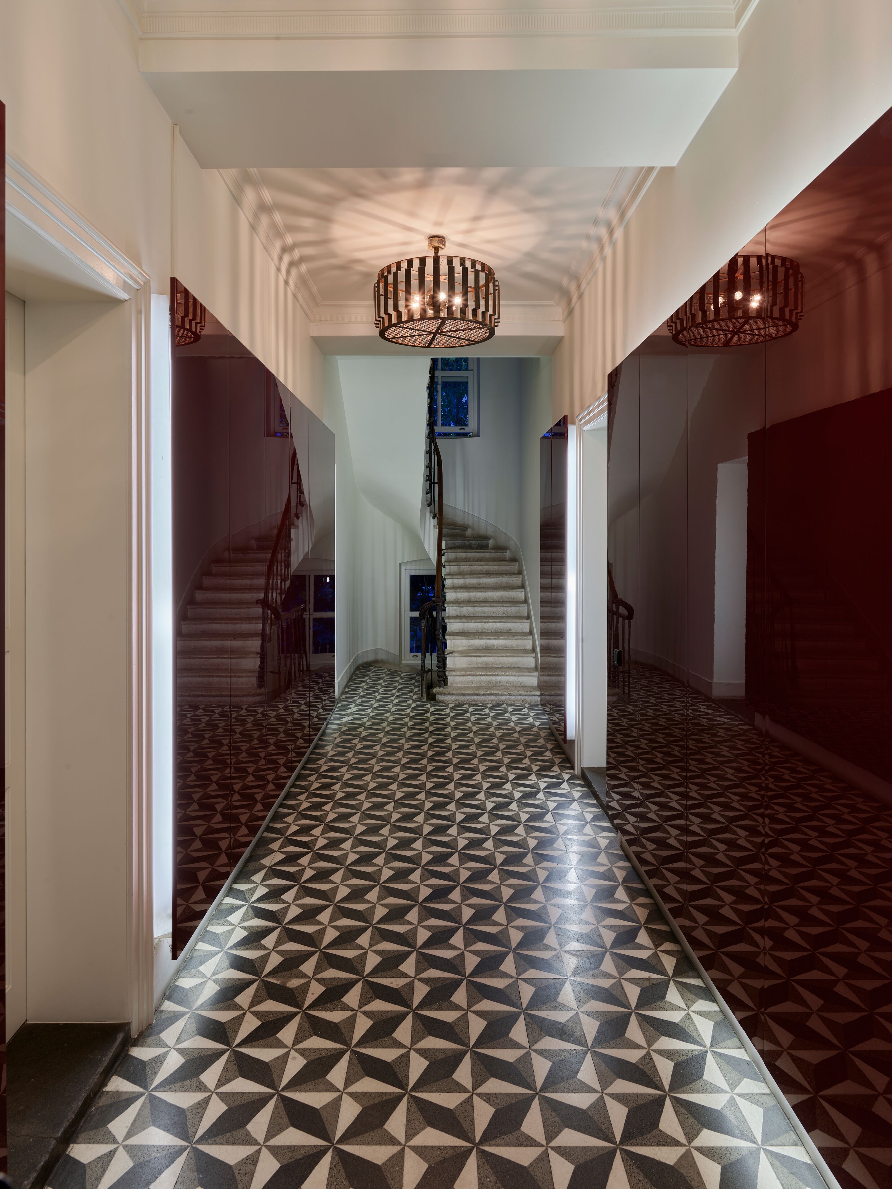 Un pasillo con suelo de diseño geométrico, una escalera y un candelabro.