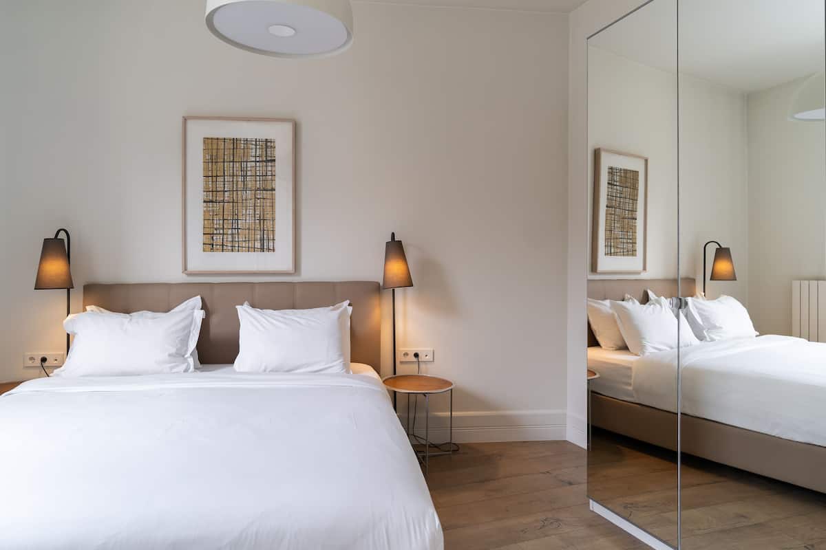 A modern hotel room with a large bed, two bedside lamps, a small round table, and a large mirror.