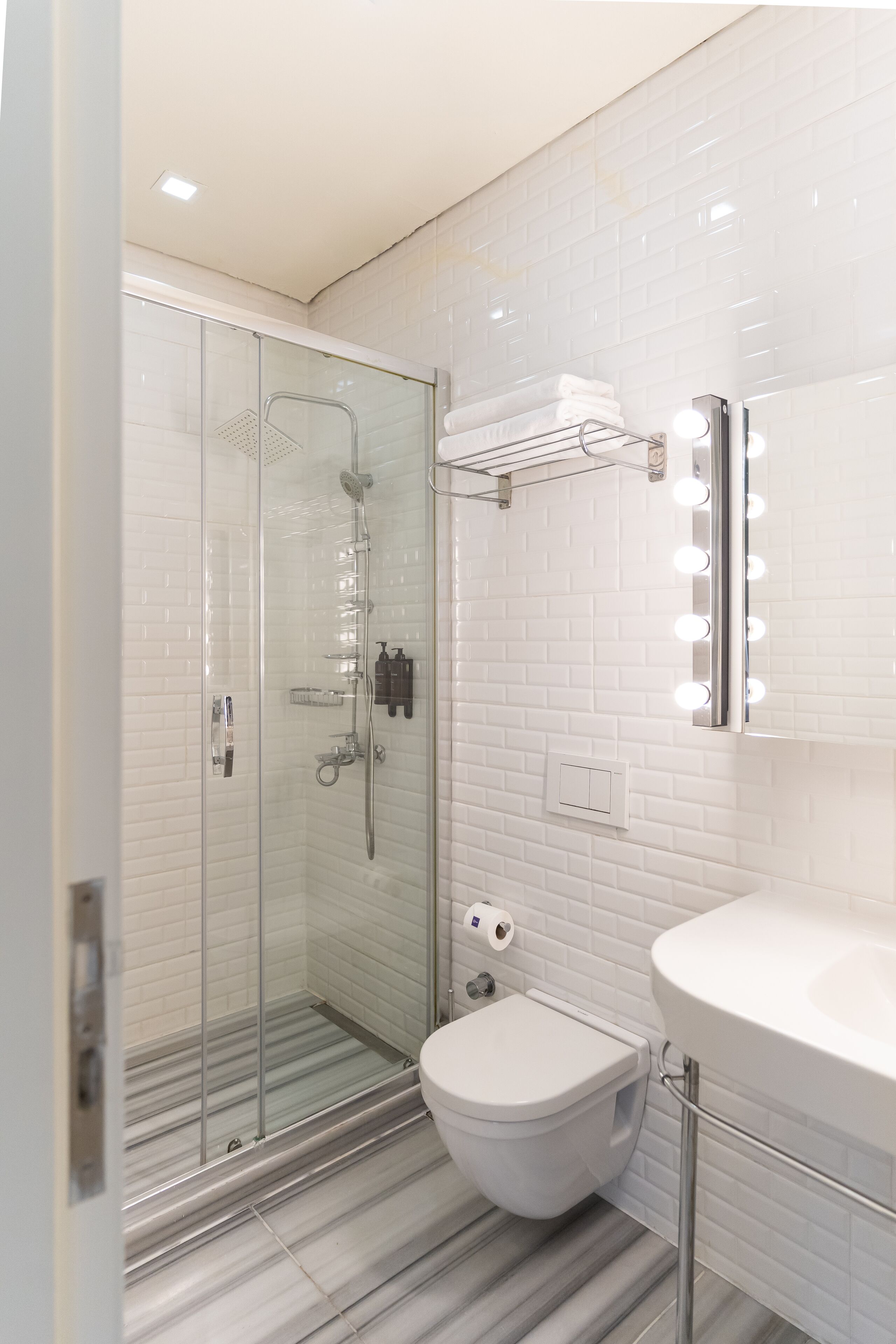 A modern bathroom with a glass-enclosed shower, a white toilet, and a vanity with a mirror and lights.