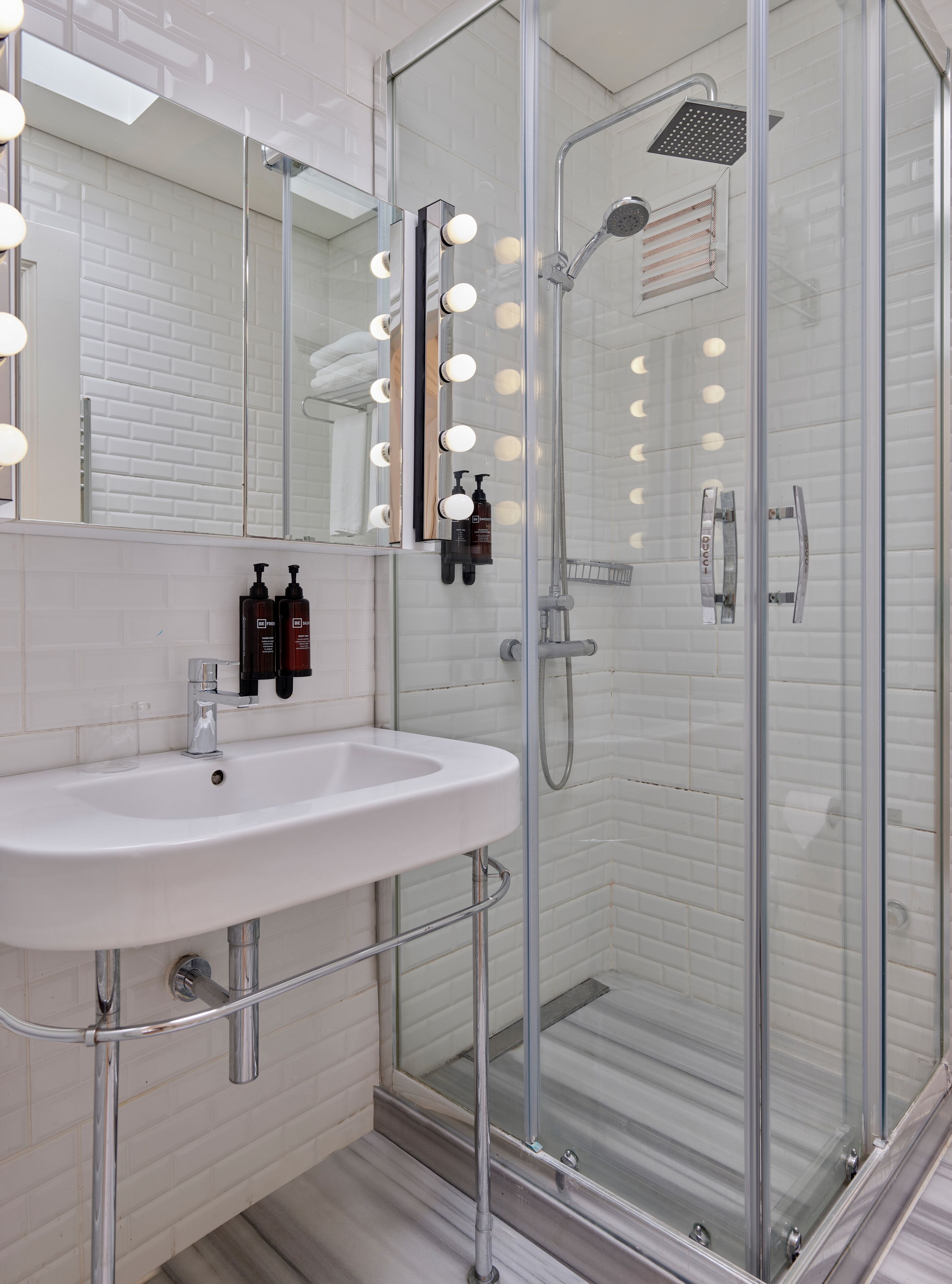 A modern bathroom with a glass shower enclosure, a white sink, and a mirror with lights.