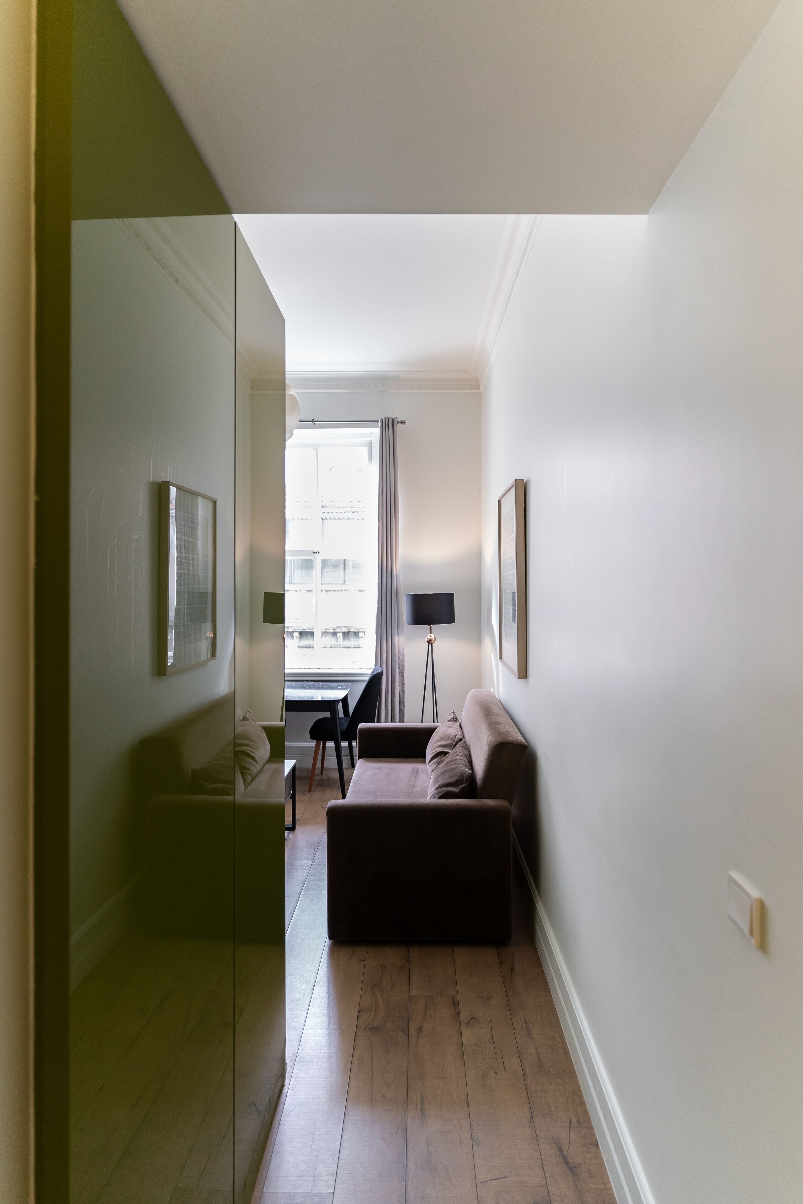 A narrow hallway with a glass partition, a dark brown sofa, a small table, and a lamp.