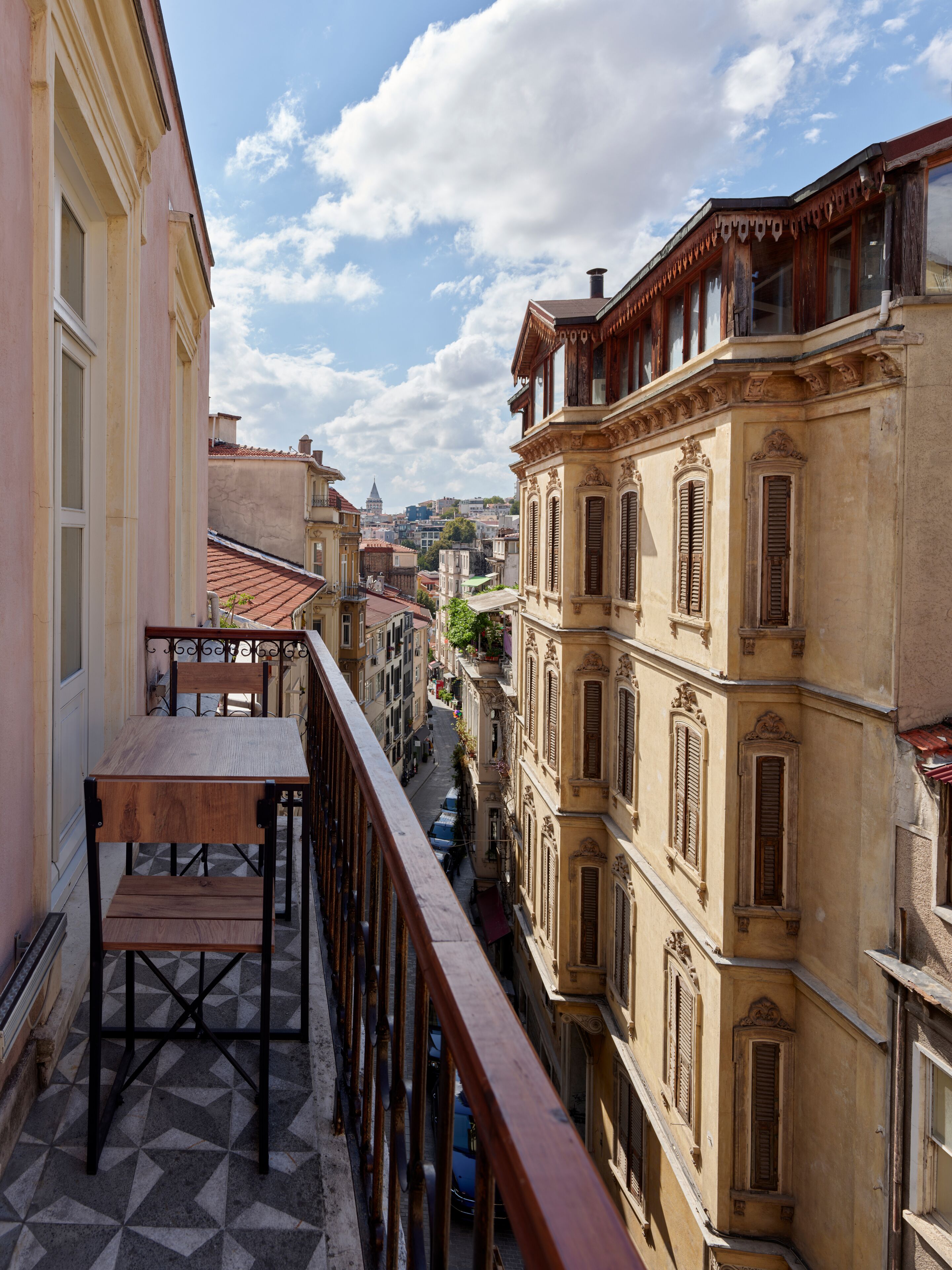 A balcony with a wooden table and chairs, overlooking a narrow street lined with historic buildings.