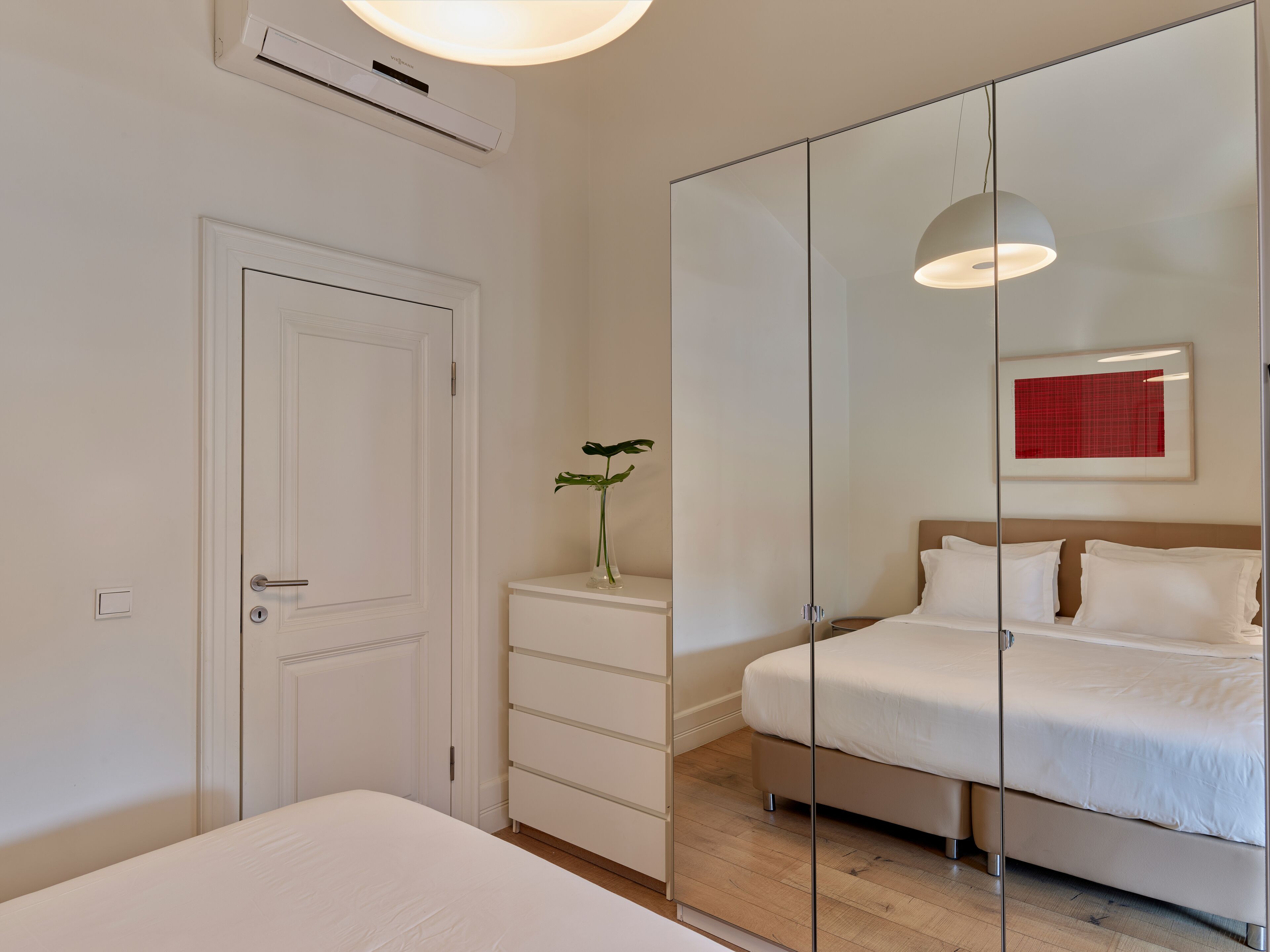 Een moderne slaapkamer met een bed, een dressoir, een spiegel en een wandairconditioner.