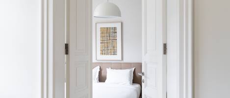 Un pasillo que conduce a un dormitorio con una cama, una lámpara colgante y un cuadro en la pared.