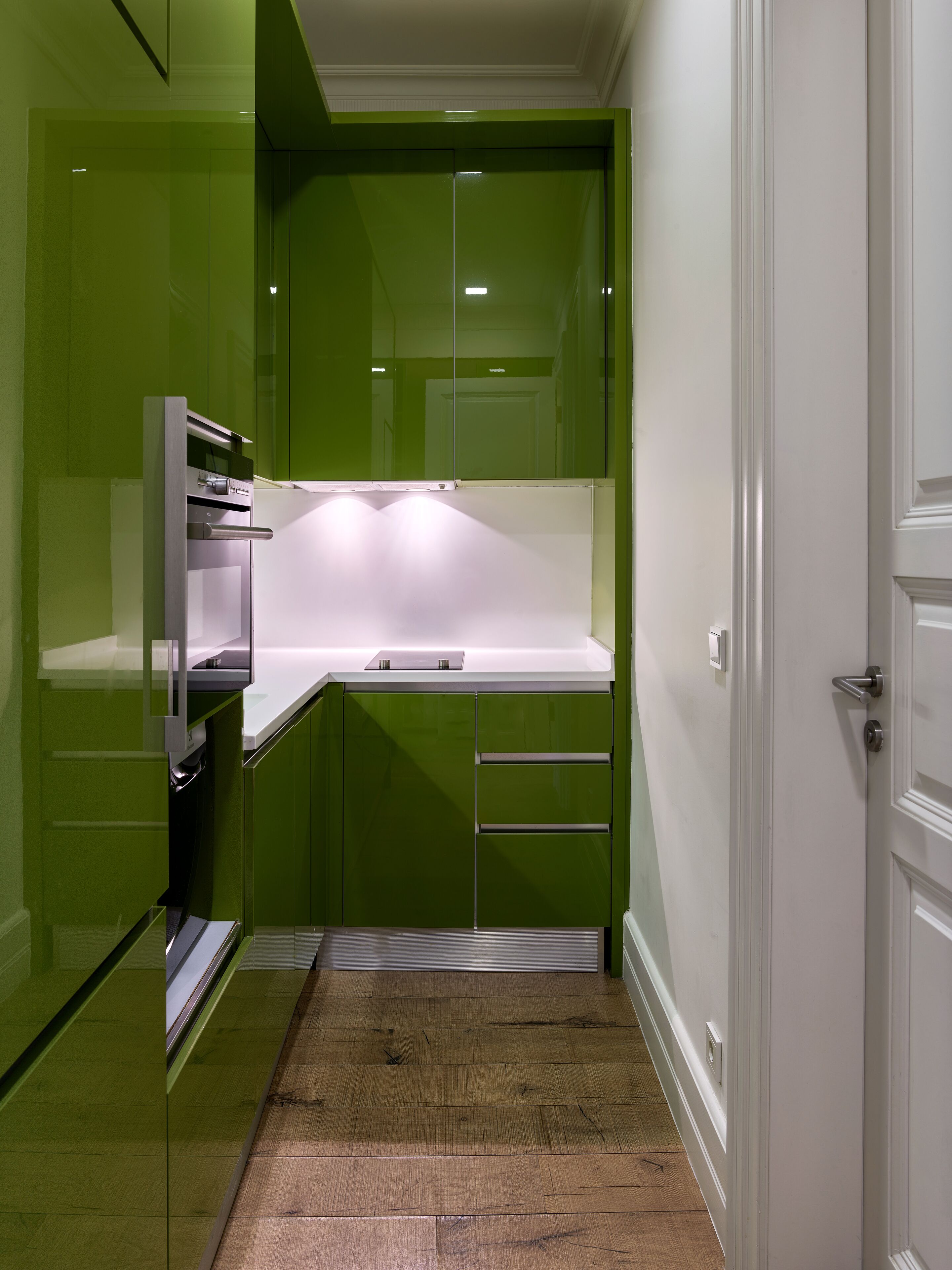 A compact kitchen with green cabinets, a white countertop, and a wooden floor.