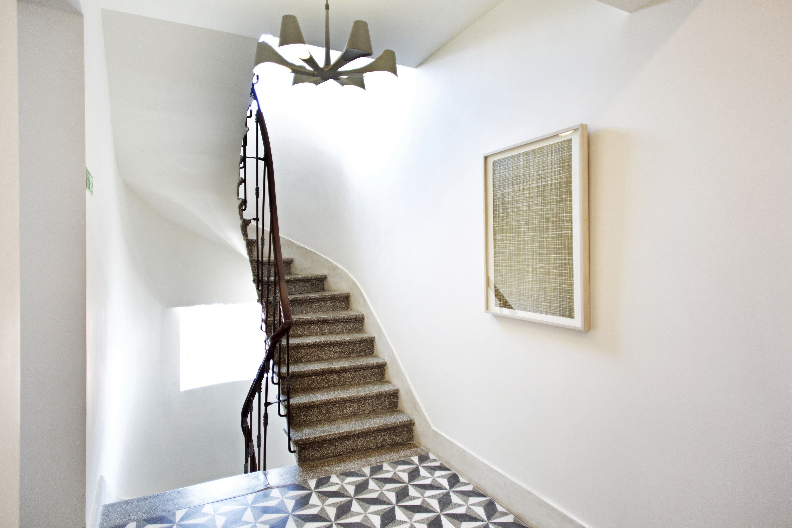 A staircase with a geometric patterned floor, a metal railing, and a wall-mounted light fixture.