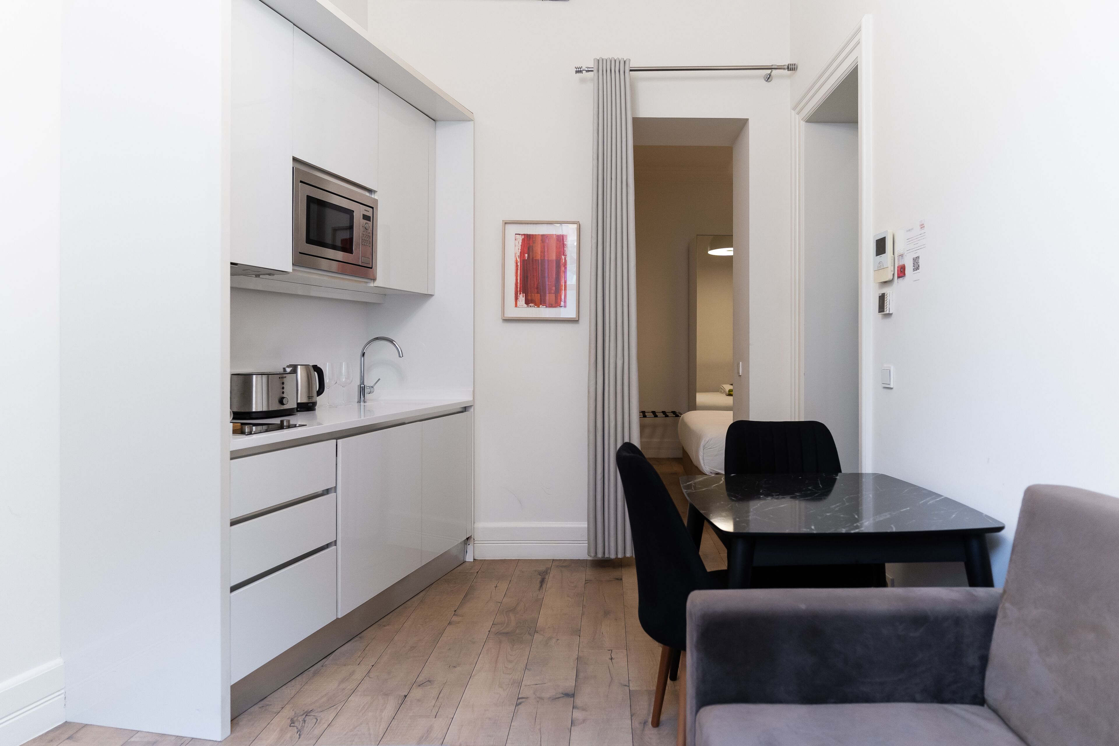 A compact kitchen with a microwave, kettle, and a dining area with a table and chairs.