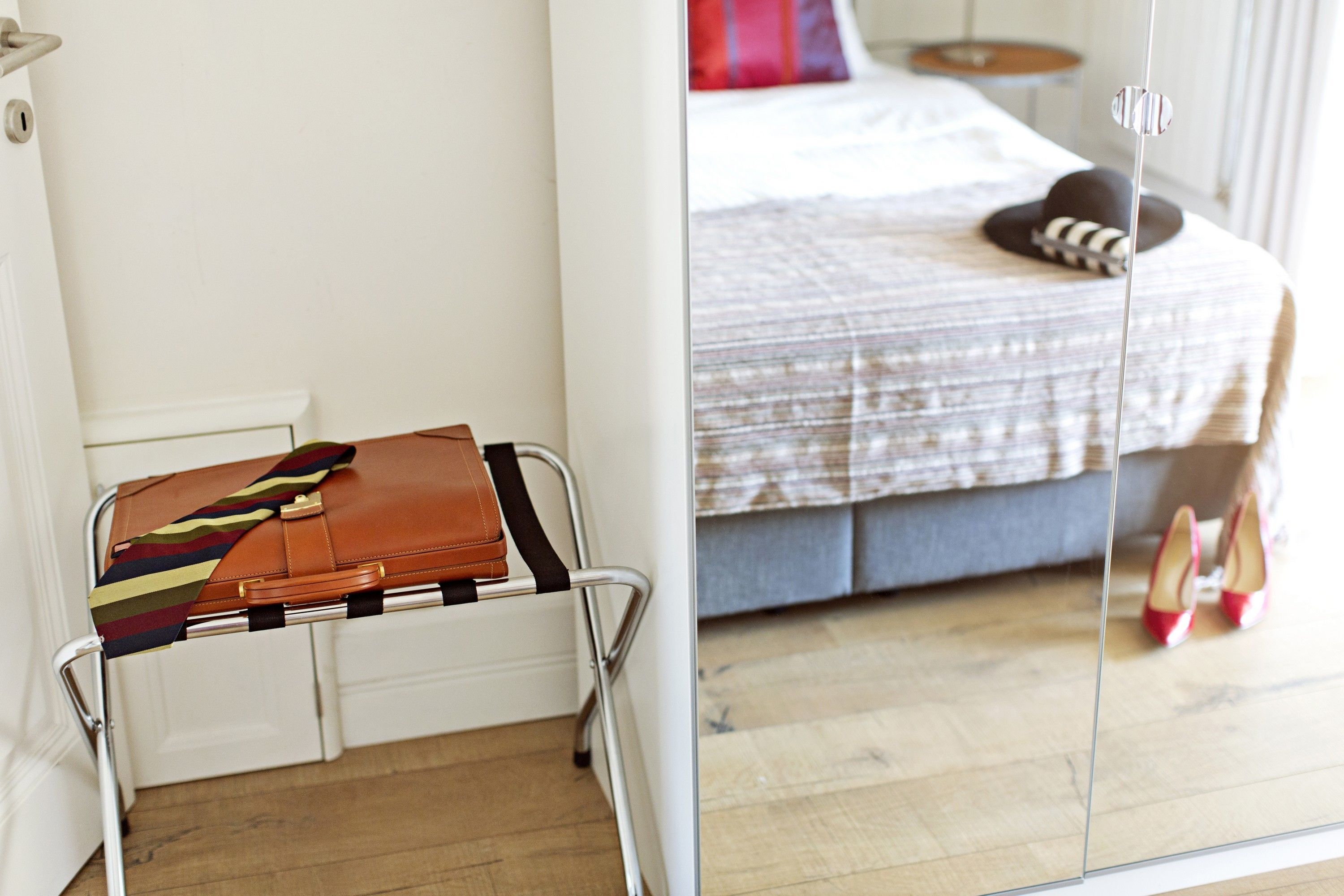 A hotel room with a bed, a suitcase on a trolley, and a pair of red high heels.