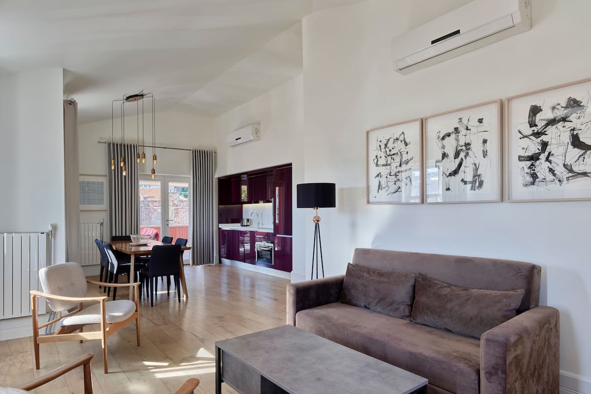 A modern living room with a sofa, coffee table, and chairs. There is a dining area with a table and chairs, and a kitchen area with a refrigerator and a black lamp.