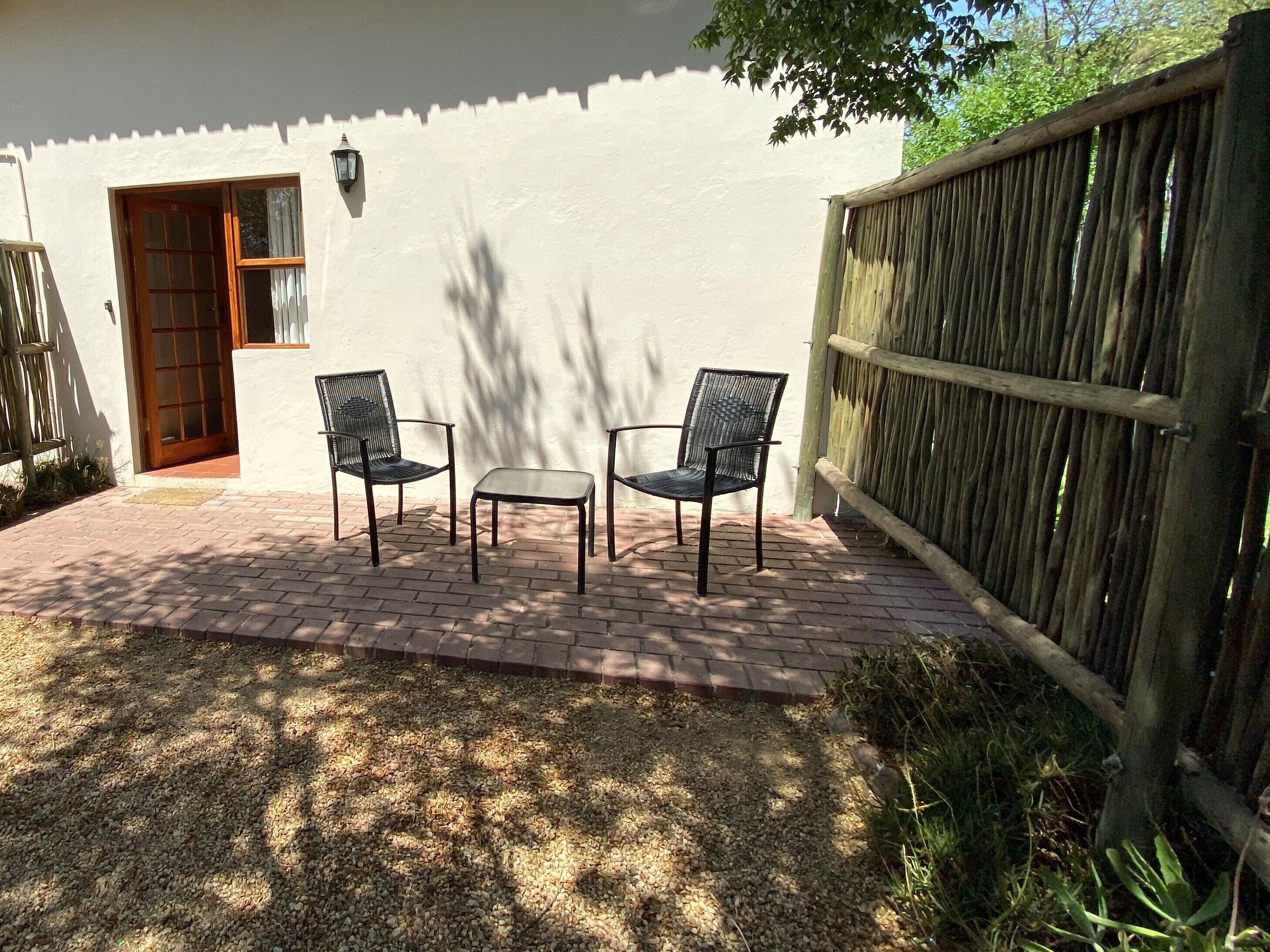 Une terrasse avec deux chaises et une table, une porte en bois et un mur blanc.