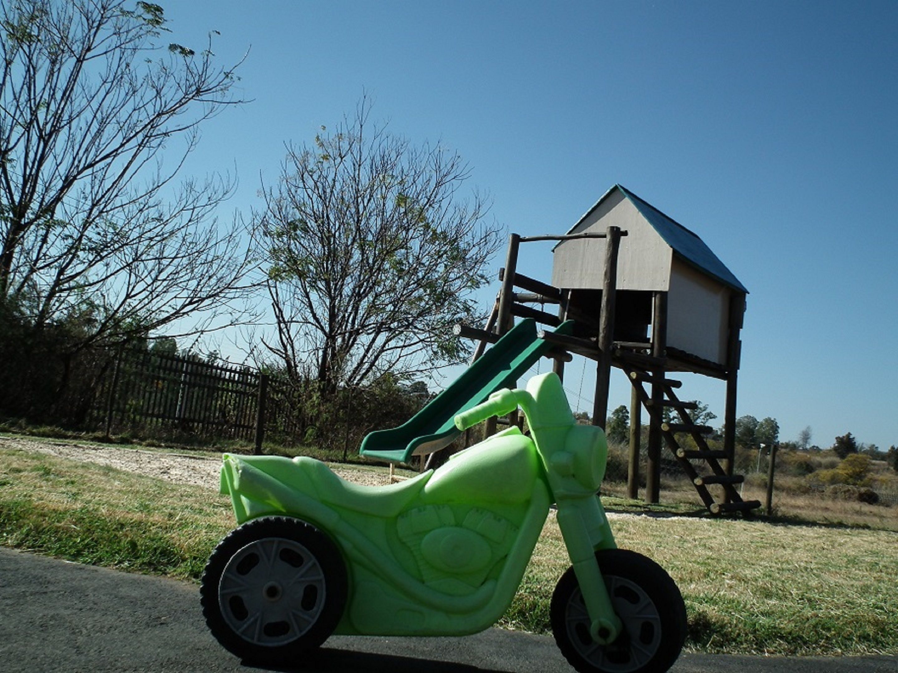 A green toy motorcycle parked on a paved surface with a playground structure in the background.