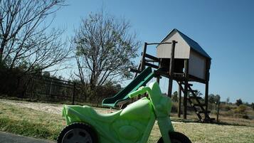A green toy motorcycle parked on a paved surface with a playground structure in the background.