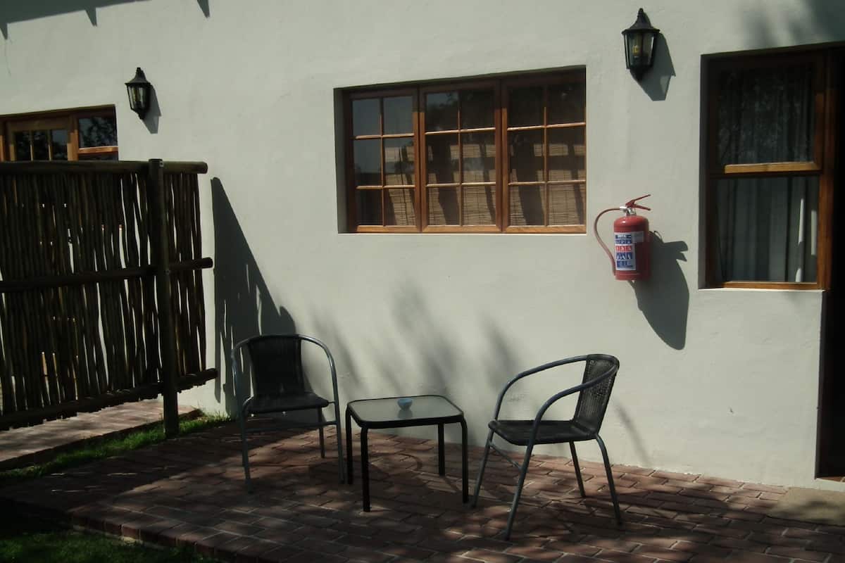 A patio with two chairs and a table, a fire extinguisher mounted on the wall, and a window with a wooden frame.