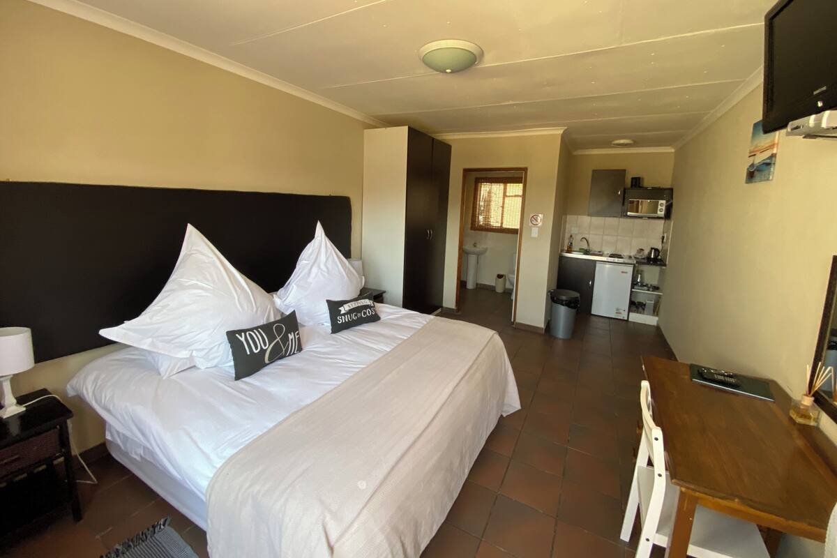 A hotel room with a bed, bedside table, lamp, and a view of the kitchen and bathroom.