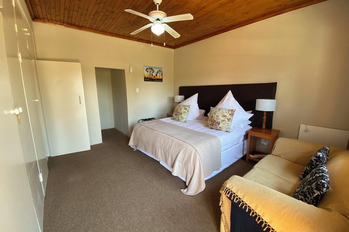 A bedroom with a bed, a nightstand, a lamp, a ceiling fan, and a door.
