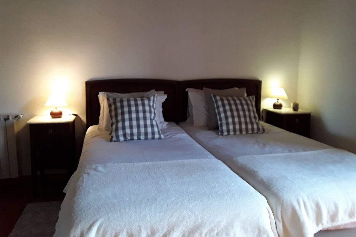 Una cama doble con dos mesitas de noche, cada una con una lámpara, en una habitación de paredes lisas.