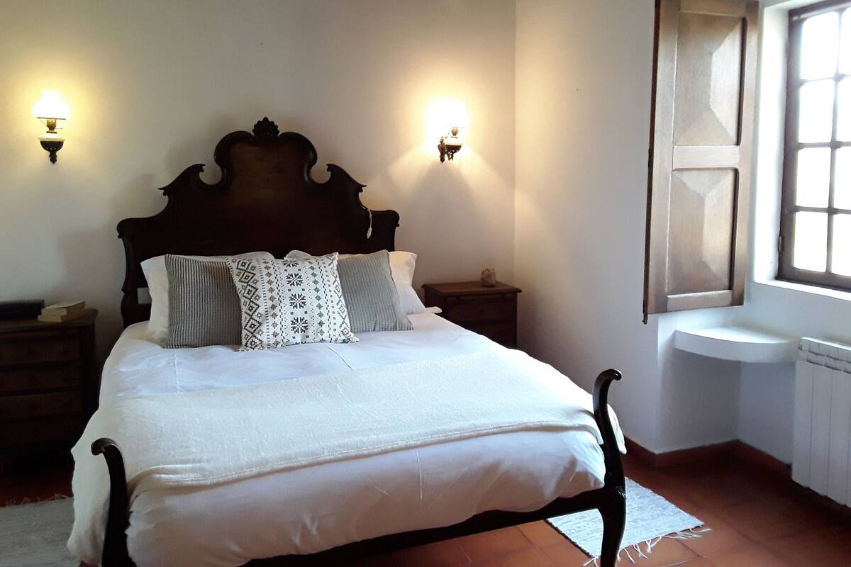 Un dormitorio con estructura de cama de madera, ropa de cama blanca, dos mesitas de noche y lámparas de pared.