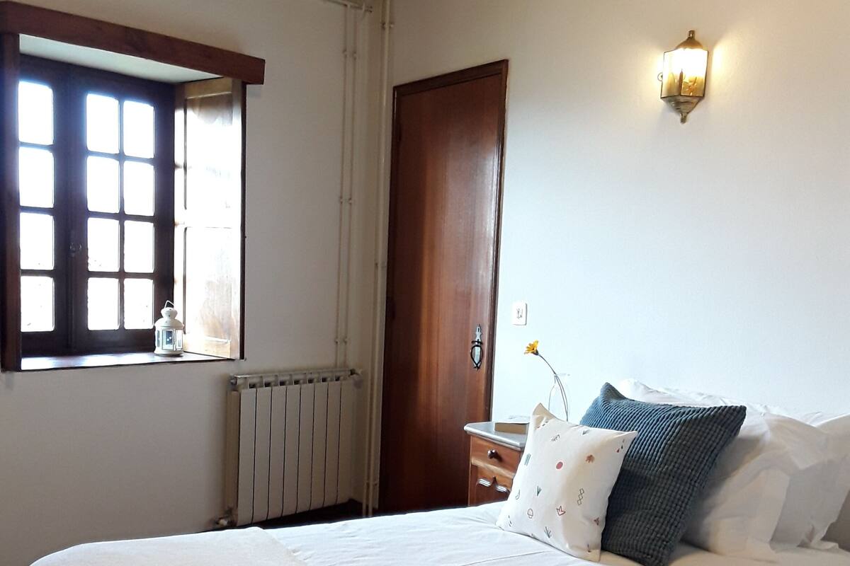 Un dormitorio con dos camas, una ventana con persianas, un radiador y una lámpara fijada a la pared.