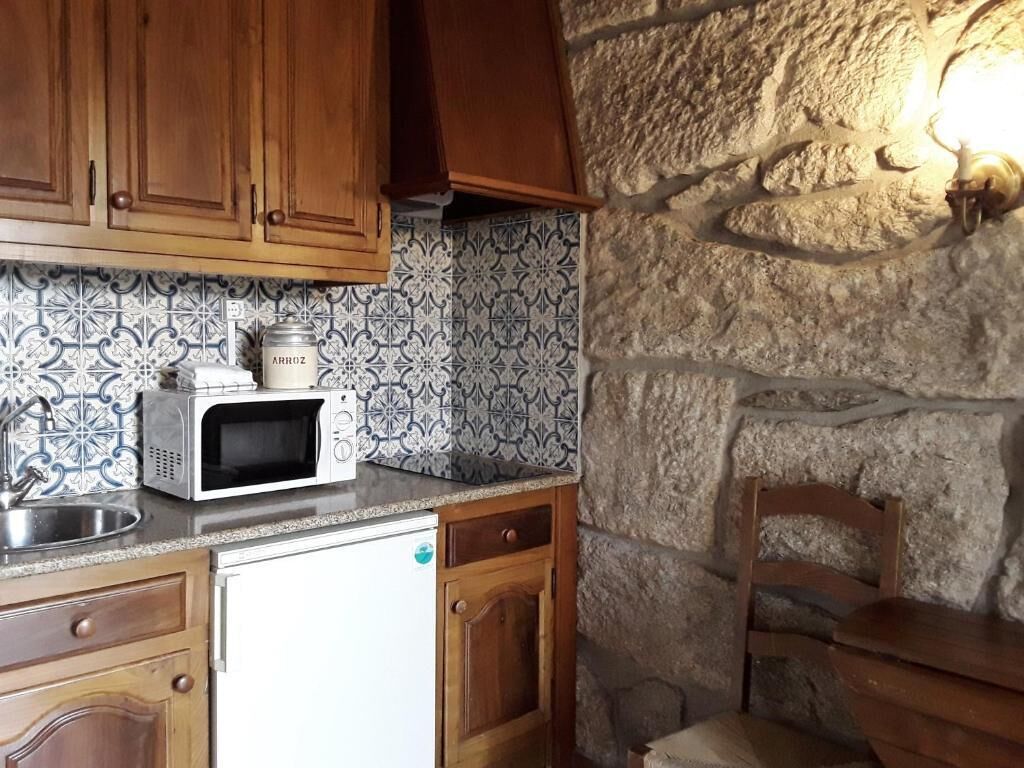 Una cocina con microondas, refrigerador, gabinetes de madera, pared de piedra y un lavamanos.