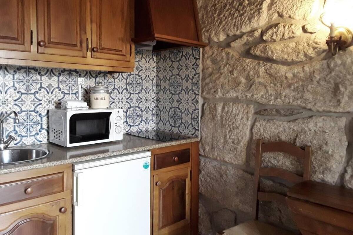 Una cocina con microondas, refrigerador, gabinetes de madera, pared de piedra y un lavamanos.