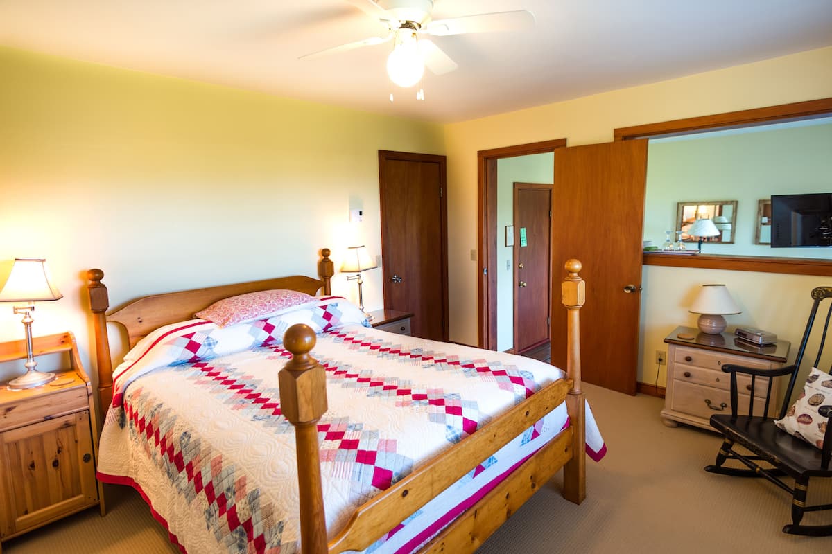 Ein Schlafzimmer mit einem hölzernen Bett, Nachttischen, einer Kommode, einem Schaukelstuhl und einem Deckenventilator.