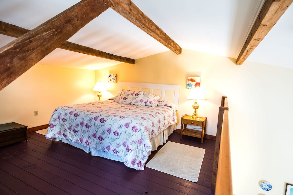 Ein Schlafzimmer mit Holzboden, einem Bett mit Blumenmuster-Bettwäsche, zwei Nachttischlampen und einem Nachttisch aus Holz.