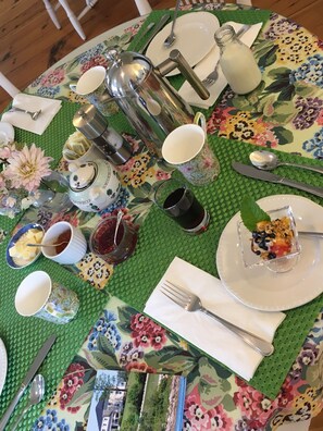 A table set with a floral tablecloth, various dishes, a teapot, and a glass of juice. - Bayview Pines Country Inn (Indian Point)