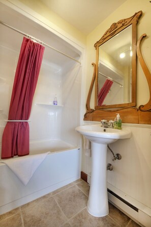 A bathroom with a bathtub, a sink, a mirror, and a shower curtain. - Bayview Pines Country Inn (Indian Point)