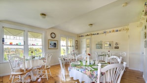 Une salle à manger avec une table en bois dressée pour six personnes, entourée de chaises blanches.