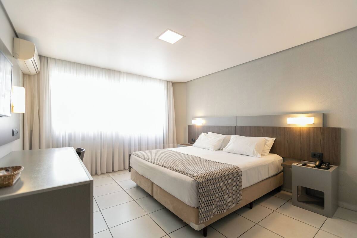 Ein modernes Hotelzimmer mit einem großen Bett, Nachttischen, einem Schreibtisch und einem Fenster mit Vorhängen.