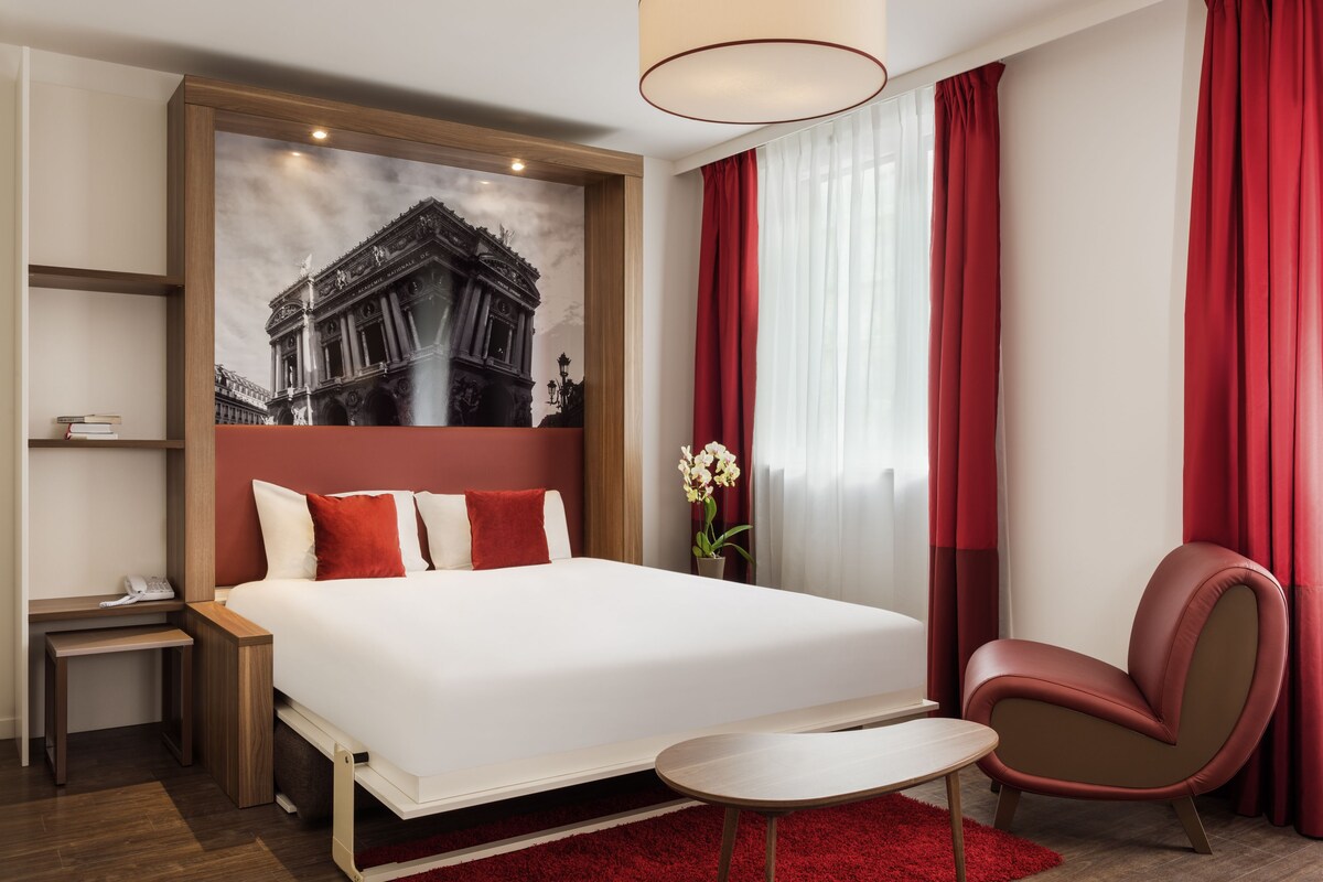 A hotel room with a large bed, a desk, a chair, and a red carpet.