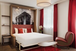 Habitación de hotel con una cama grande, un escritorio, una silla y una alfombra roja.
