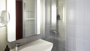 A modern bathroom with a white sink, a mirror, and a glass-enclosed shower. - Aparthotel Adagio Birmingham City Centre (Birmingham)