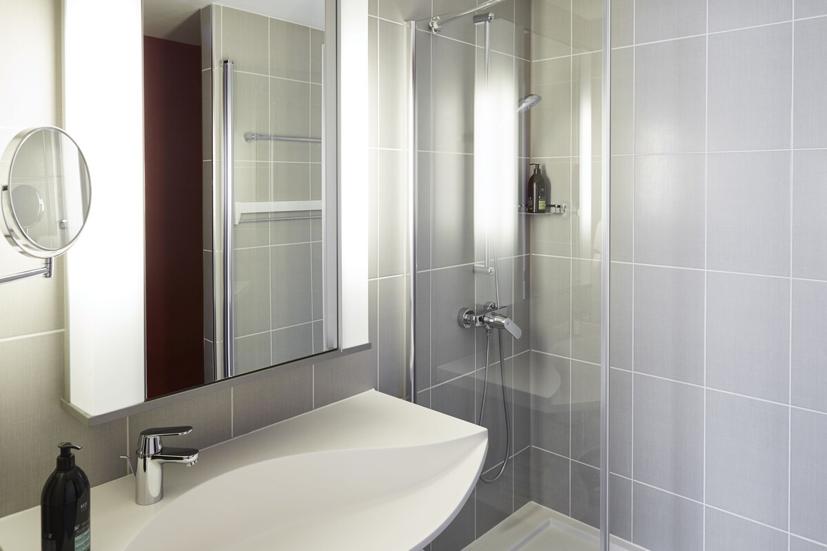 A modern bathroom with a white sink, a mirror, and a glass-enclosed shower.