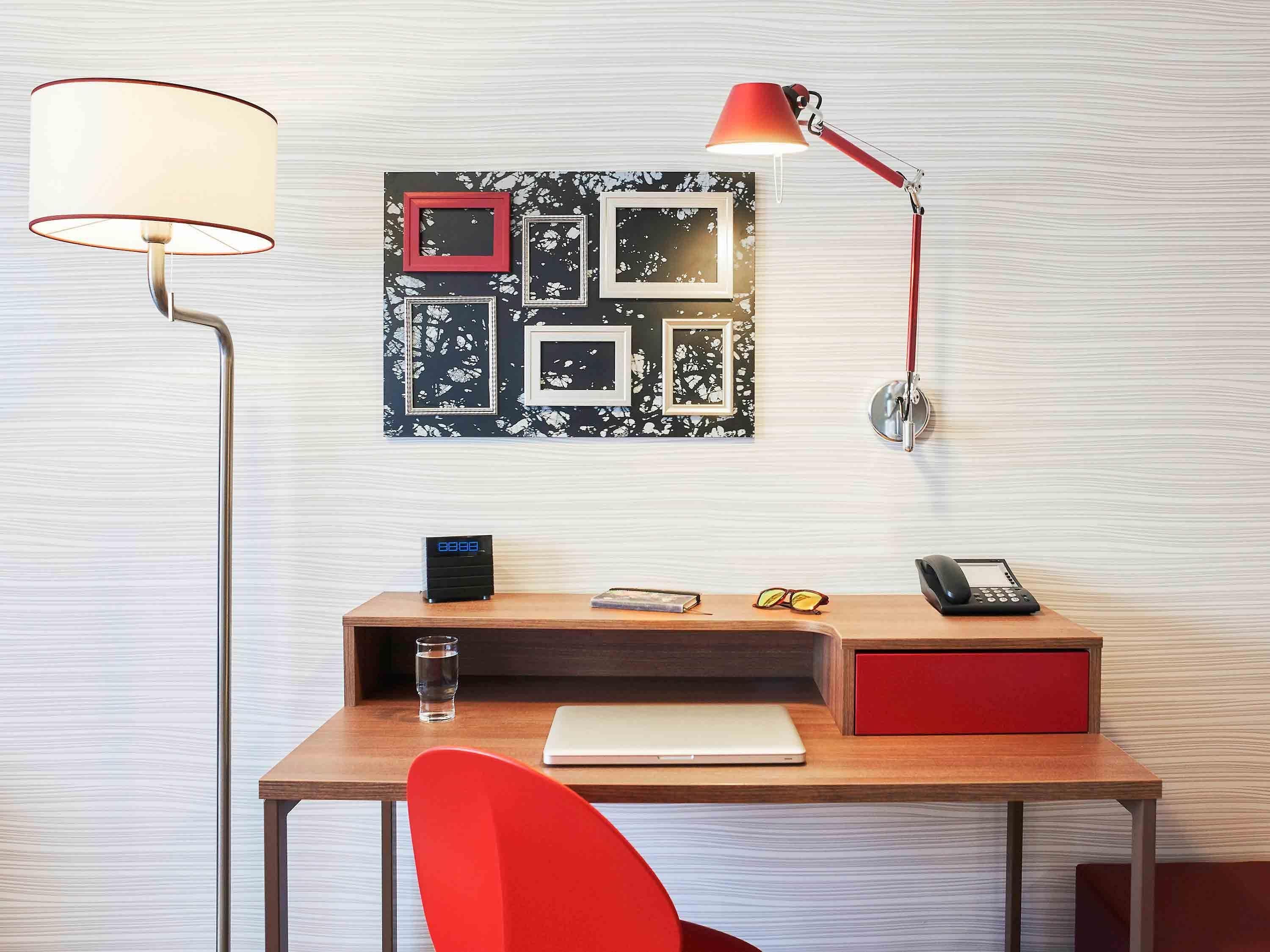 A desk with a laptop, a red chair, a lamp, a clock, and a wall-mounted phone.